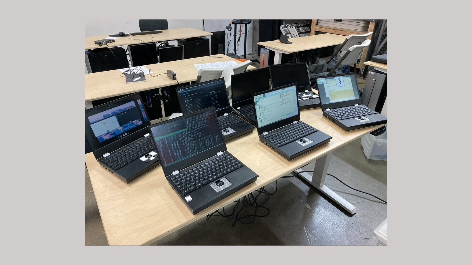 Seven MNT Reform laptops on a table together in a hackerspace