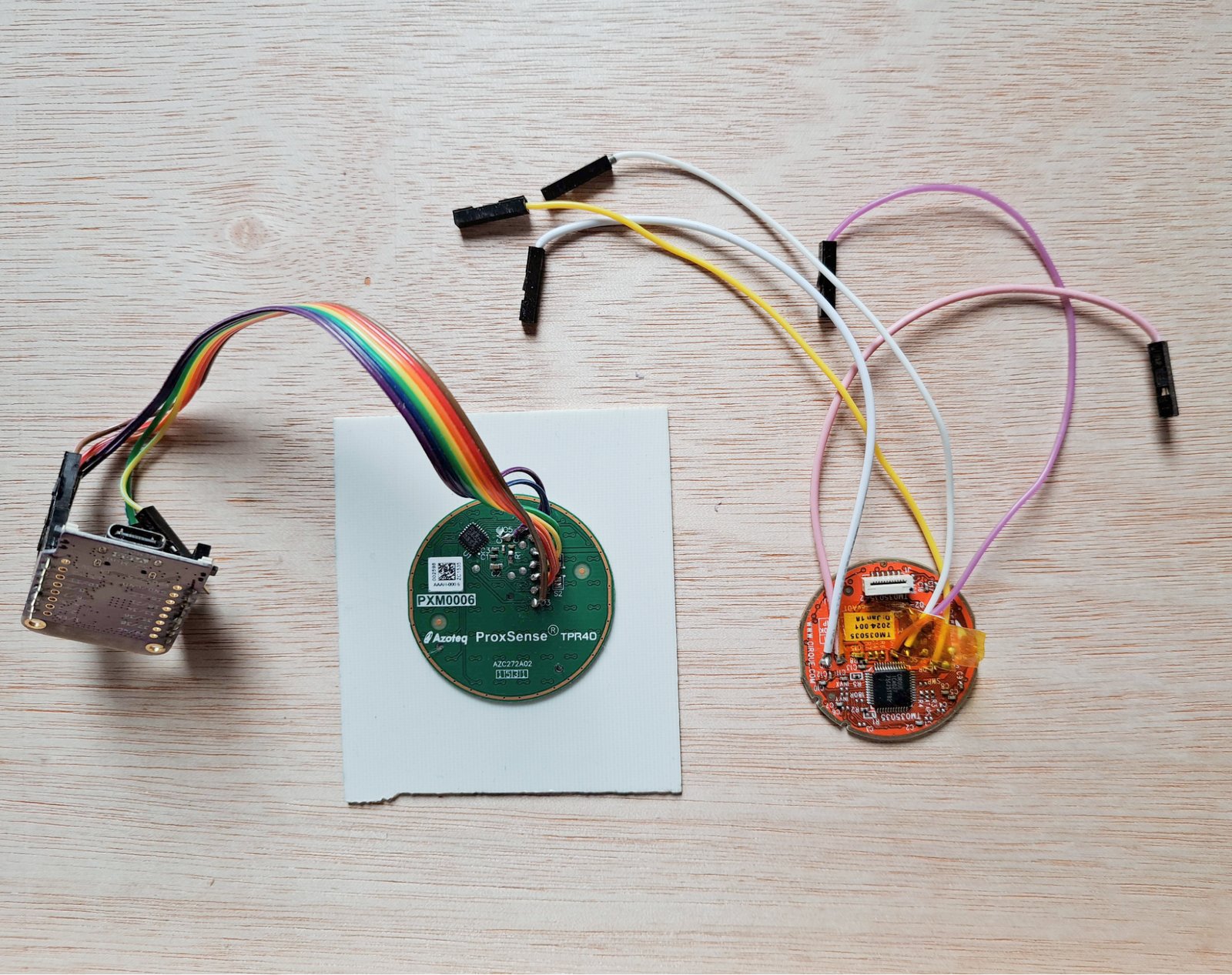 A photo of two trackpad modules. On the left: An Azoteq Proxsense trackpad module stuck to a scrap piece of FR4, wired up to a microcontroller On the right: A Cirque Glidepoint trackpad module with some jumper leads soldered to it