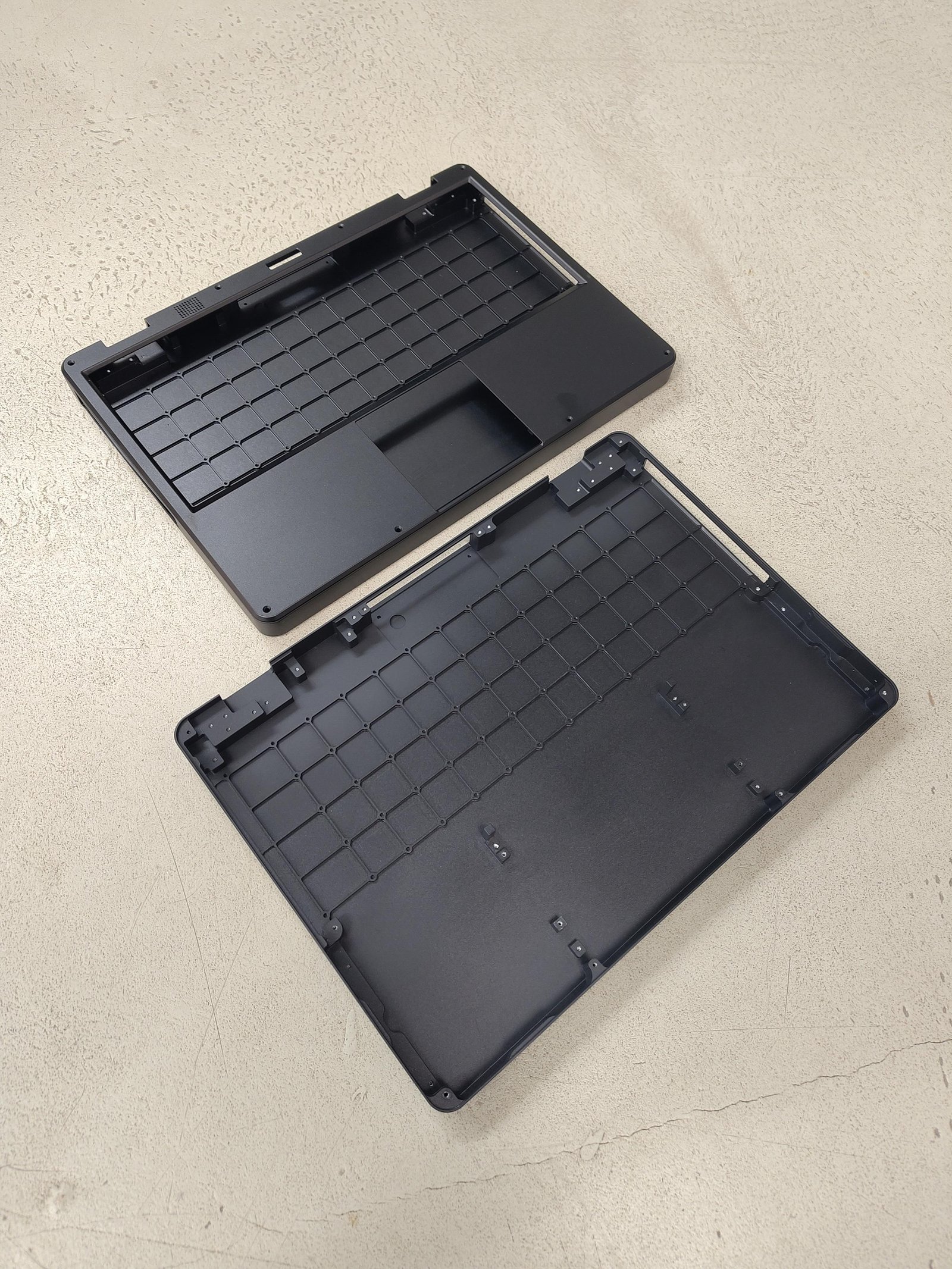 mnt reform next bottom cases, one opened, one with the frame/bezel for keyboard and trackpad on top. black bead blasted milled aluminum